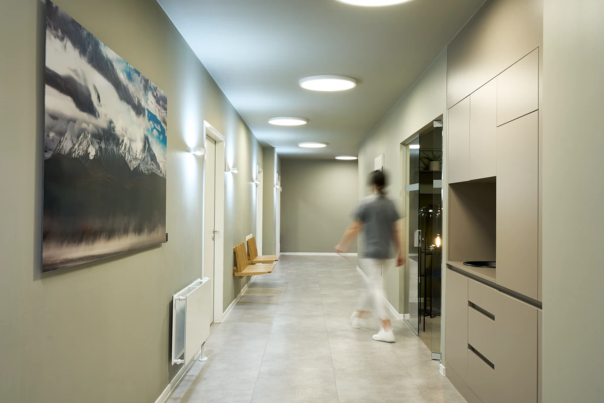 Moderner Flur der RKM 740 Facharztklinik in Düsseldorf mit Kunstwerk, Sitzbank und Mitarbeiterin im Bewegungsmoment