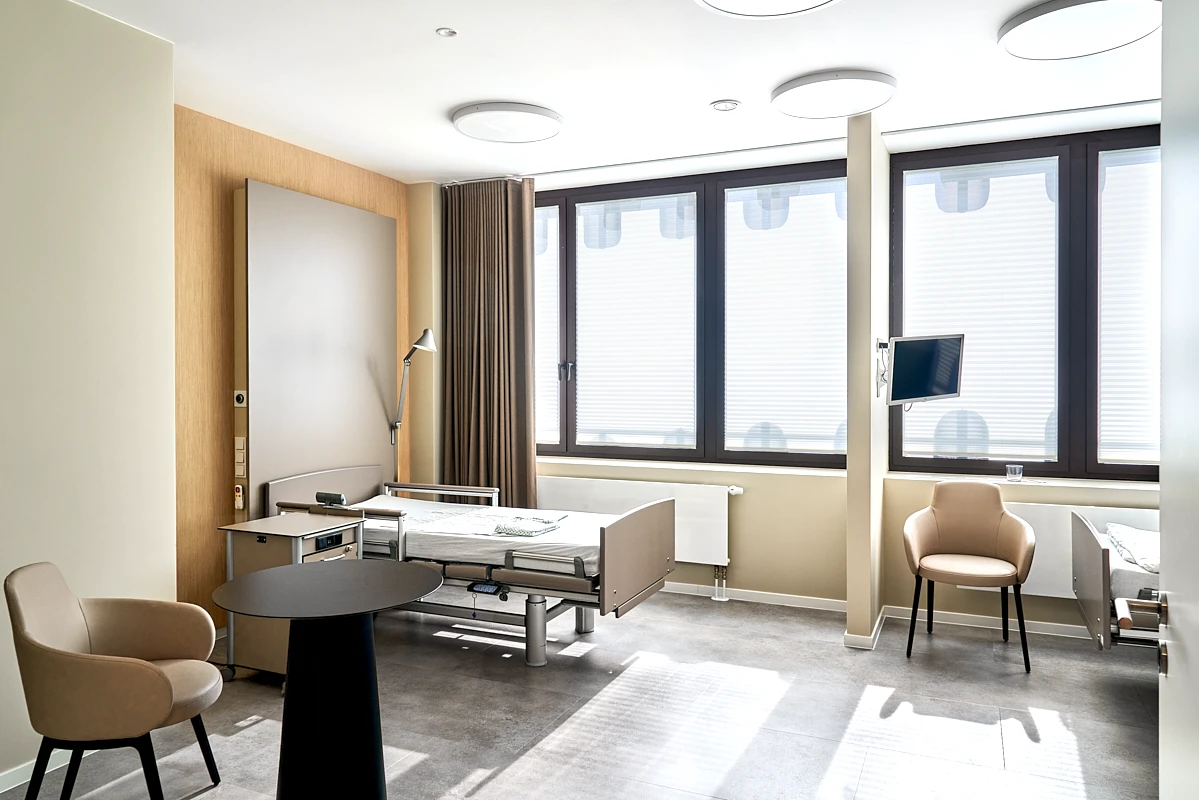 Helles Patientenzimmer der RKM 740 Facharztklinik in Düsseldorf mit großem Fenster, Sitzbereich und moderner Ausstattung